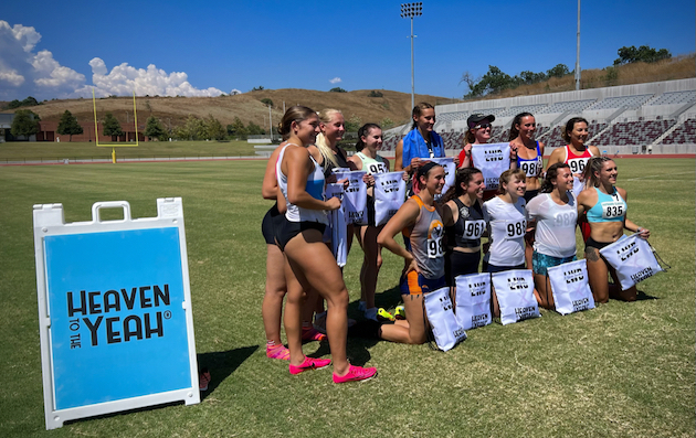 Group photo of Women's Decathlon athletes on a grass field at a stadium, with a sign at left for the Heaven to the Yeah organization. Photo credit: Collin Brewer